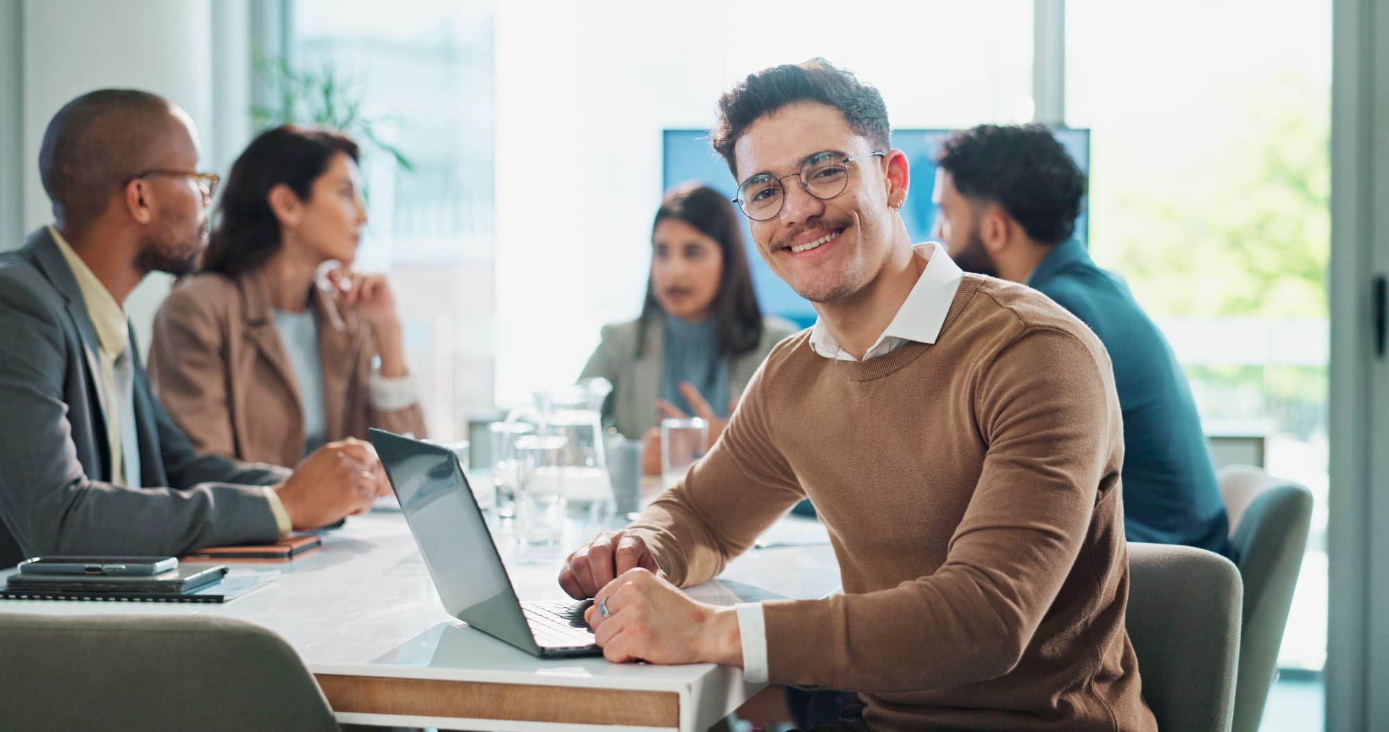 A finance team in a meeting, one colleague smiling at the camera over a laptop